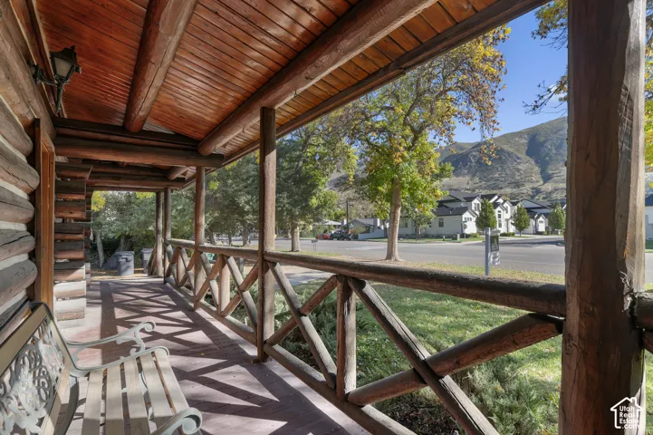Covered porch featuring natural log construction, timber support beams, wood-plank ceiling, and a rustic log railing