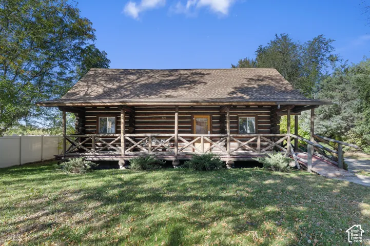 Log exterior cabin featuring a full-width covered porch with rustic wood railing, shingle roof, and wooden ramp access