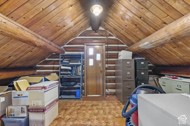 Exposed log walls, vaulted wood-plank ceiling, structural timber beams, and a wood entry door with glass inserts