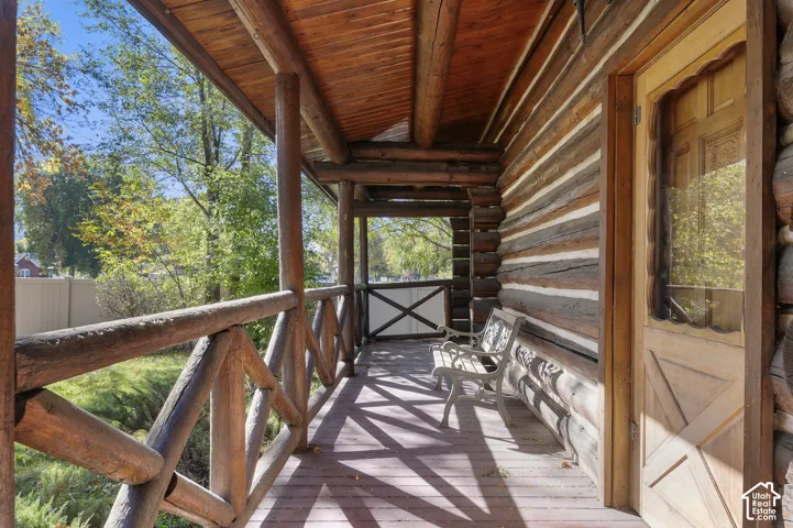 Covered log cabin porch featuring exposed timber log walls, a rustic log rafter ceiling, a sturdy log-style railing, and a handcrafted wooden entry door