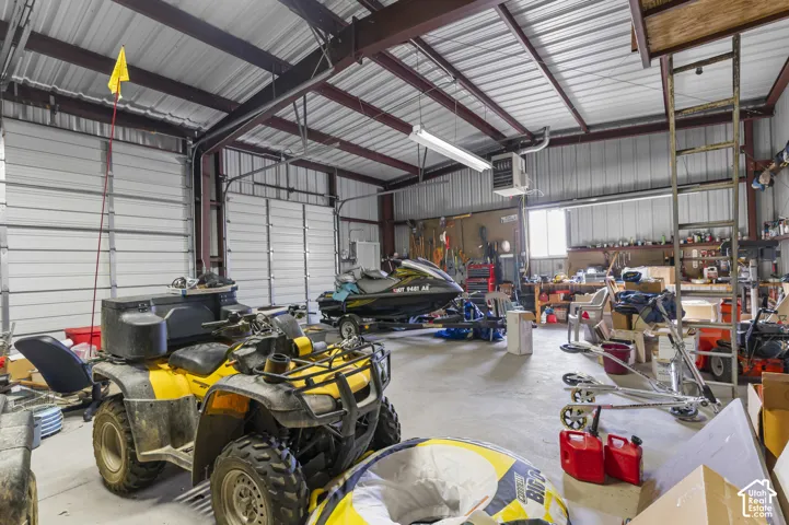 Expansive workshop featuring high ceilings with exposed steel beams, concrete flooring, multiple overhead doors, and a built-in metal ladder