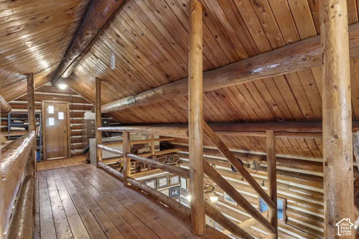 Interior loft featuring tongue-and-groove wood paneling, exposed log structural beams, log railing, and wood-finish flooring