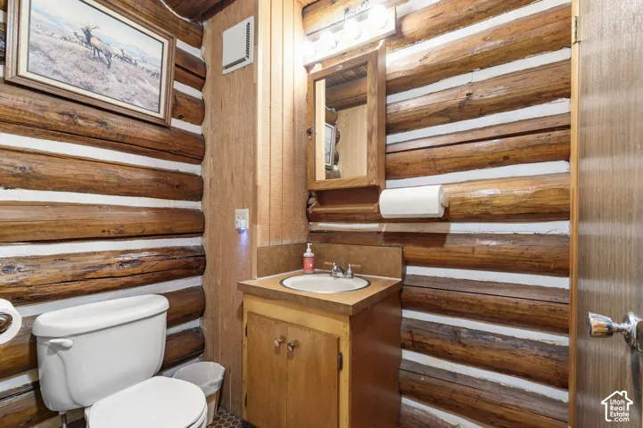 Log-hewn wall construction with white mortar chinking, wood vanity cabinet, inset sink basin, and surface-mounted medicine cabinet with integrated vanity lighting