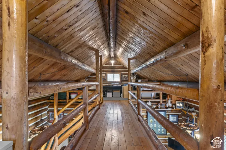 Vaulted ceiling with exposed log beams, tongue-and-groove wood paneling, wood flooring, and log-style railing