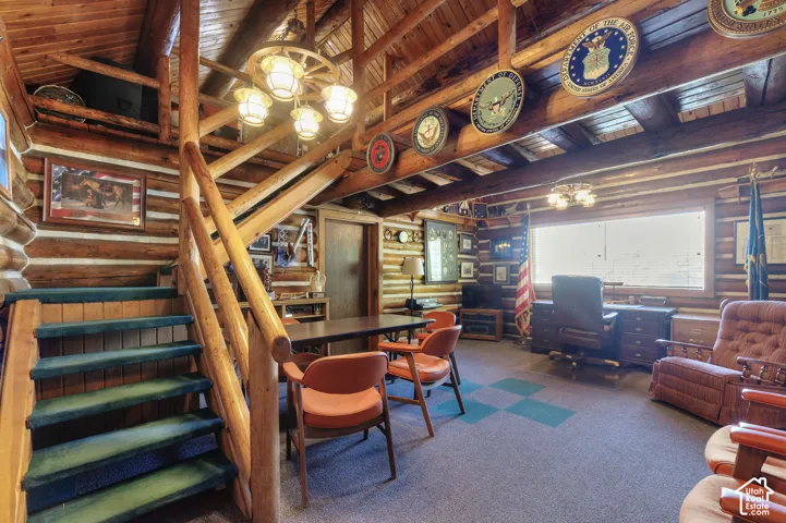 Exposed log walls, vaulted wood-beam ceiling, wagon wheel-style chandelier, and timber staircase with a matching log handrail