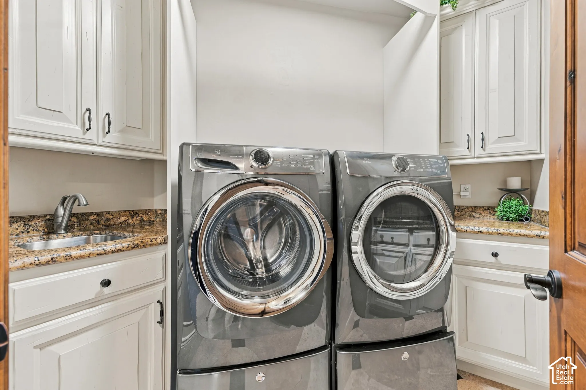 Laundry room featuring white cabinetry, stone-finish countertops, an undermount sink with a gooseneck faucet, and built-in upper storage.