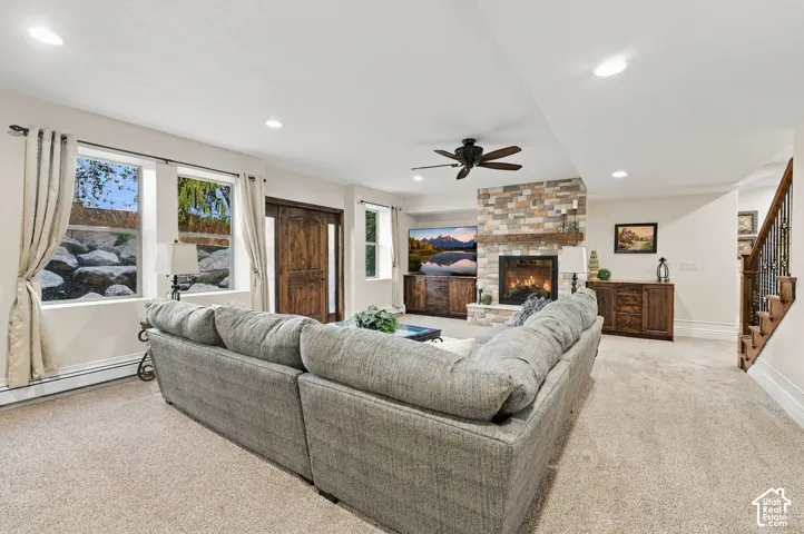 Full-height stone fireplace with timber mantel, built-in cabinetry, recessed ceiling lighting, ceiling fan, and staircase with metal balusters.