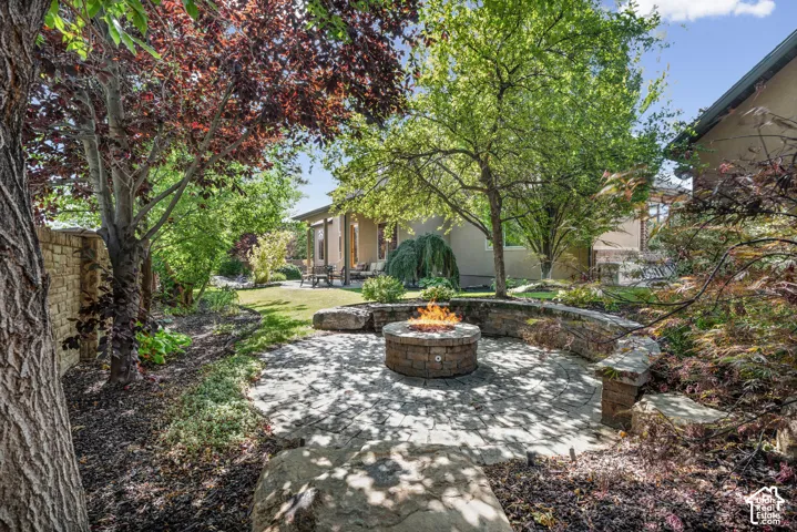 Backyard featuring a circular stone patio, integrated stone fire pit, curved stone seating wall, mature trees, and a retaining wall.