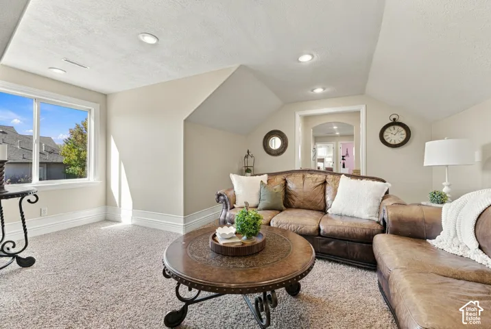 Sloped ceilings with recessed lighting, carpeted flooring, and a large window.