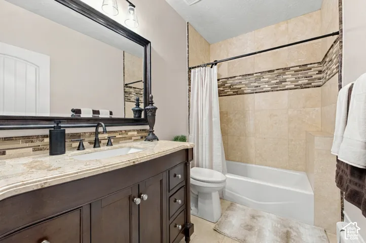 Dark-finish cabinetry vanity with stone-surfaced countertop, rectangular undermount sink, framed wall mirror, and shower-tub combination with decorative tile inlay.