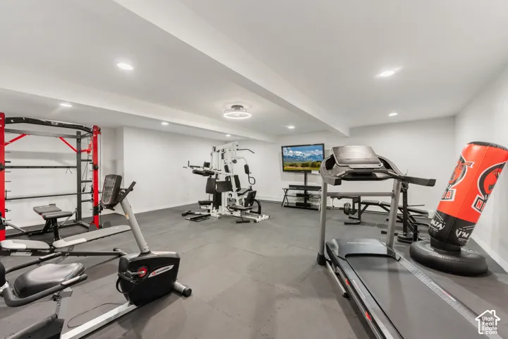 Exercise room featuring recessed lighting, a ceiling-mounted ceiling fan with light fixture, and rubberized interlocking floor tiles. TV with stand and white universal gym can stay.