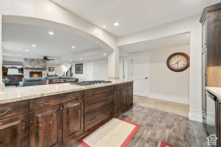 Kitchen featuring dark stained wood cabinetry, stone countertops, an integrated gas cooktop, recessed lighting, and wood-finish flooring.