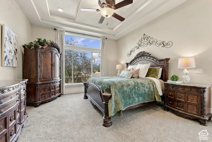 Tray ceiling, ceiling fan with integrated lighting, oversized picture window, and neutral carpeting.