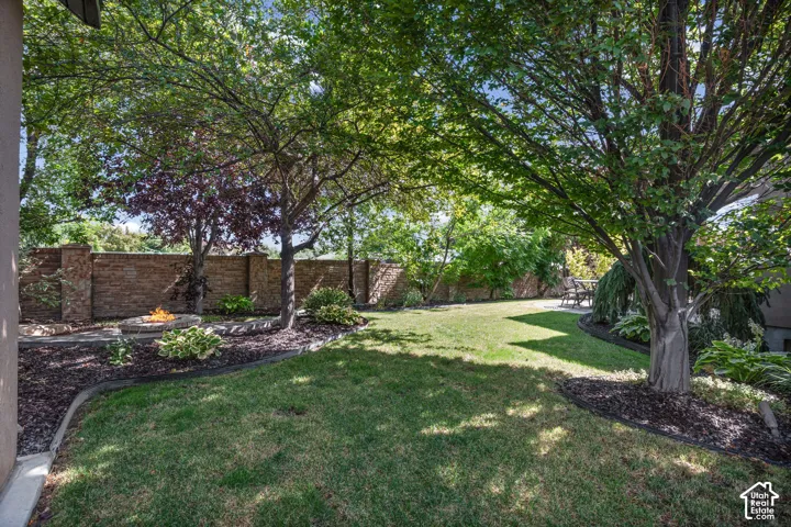 Private backyard featuring a circular stone fire pit, extensive masonry perimeter wall, mature trees, and landscaped garden beds with edging.