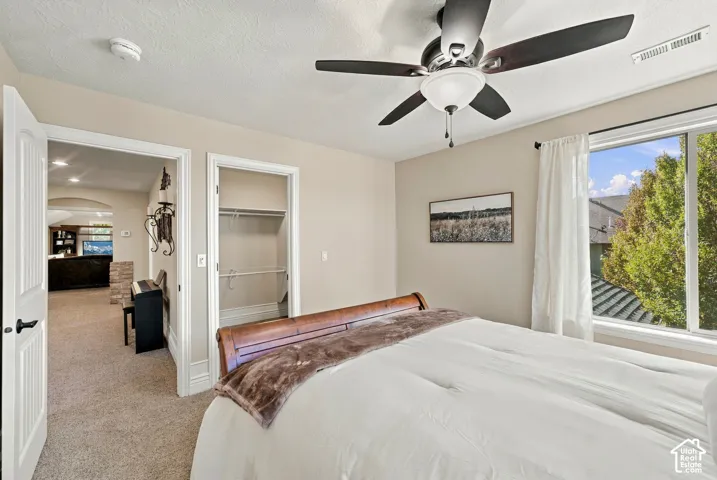 Bedroom featuring neutral wall paint, a multi-blade ceiling fan with integrated lighting, and a built-in walk-in closet.