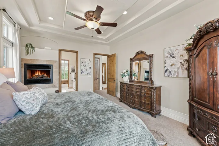Tray ceiling with recessed lighting, ceiling fan, fireplace with stone surround, and wood-finish doors.