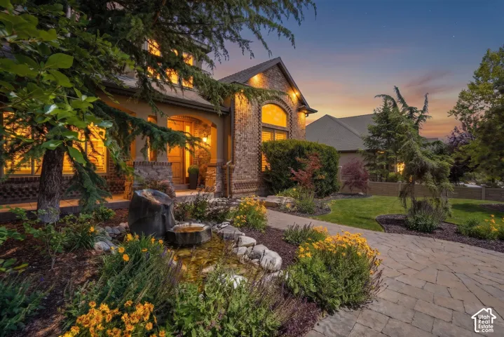 Stone exterior featuring arched windows, decorative brick detailing, a stone-paved walkway, and a landscaped rock garden with a stone water fountain. Large covered front porch.