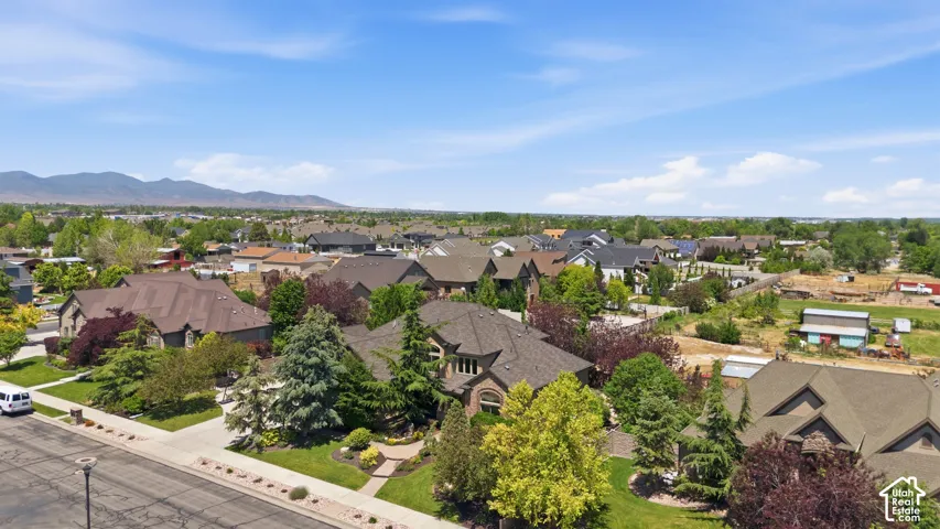 Aerial perspective featuring a residential property with a multi-gable roofline, paved driveway, landscaped grounds with mature evergreen trees, and a mountain horizon backdrop.