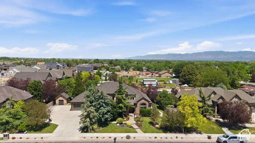 Aerial perspective featuring a multi-gabled residence with a concrete driveway, detached storage structure, manicured landscaping, and mountain backdrop.