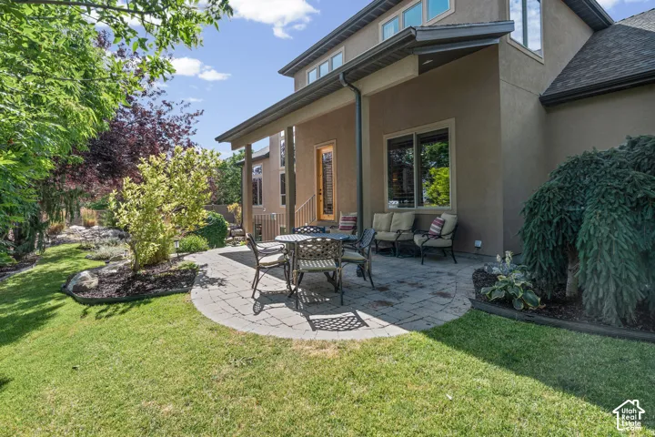 Stucco exterior with covered patio with a gas line for a BBQ, mature landscaping, and multi-level roofline.