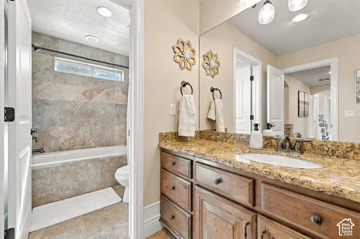 Bathroom featuring wood-finish cabinetry, stone-texture countertop with an integrated basin, large vanity mirror, and bathtub enclosure with tiled surround.