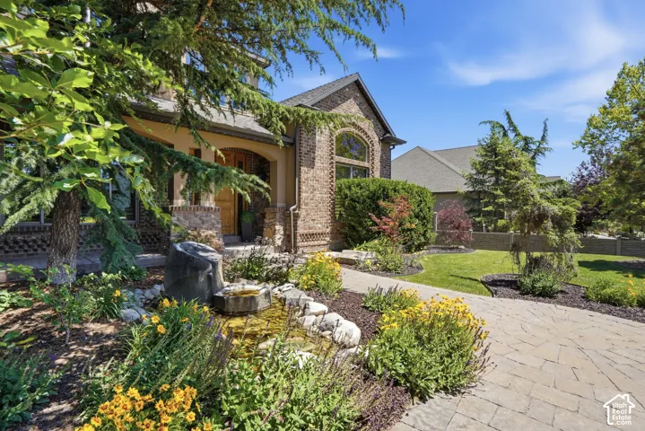Brick facade exterior featuring a covered porch entrance, arched windows, stone-paved walkway, and integrated water feature surrounded by established perennial landscaping