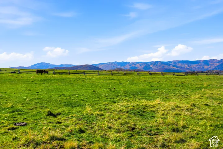 Expansive acreage featuring rolling grass pasture, split-rail wooden fencing, and a mountain backdrop