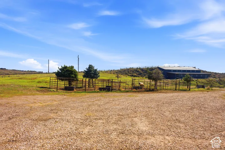 Expansive acreage featuring metal pipe fencing, equestrian pens, a gravel lot, and a large-scale metal structure