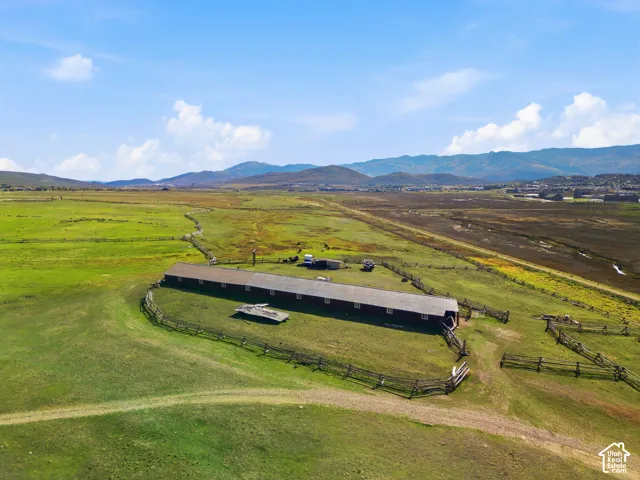 Expansive acreage featuring a long, low-profile structure with a pitched roof, enclosed by split-rail perimeter fencing and set against a prominent mountain backdrop