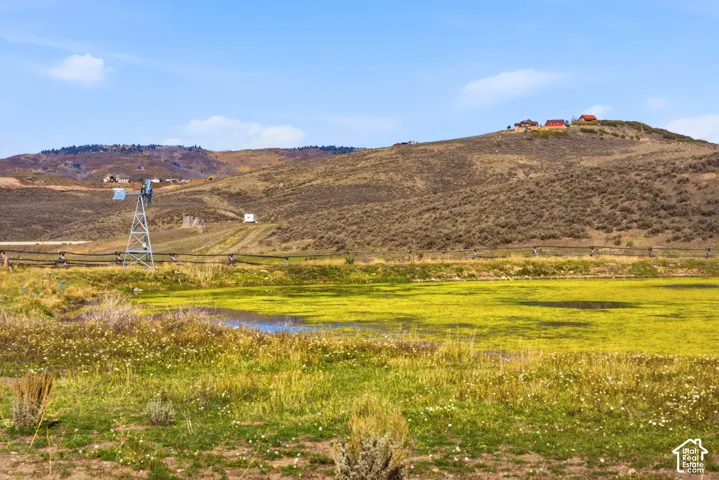 Expansive acreage featuring a natural pond, a classic windmill, post-and-rail fencing, and mountainous terrain