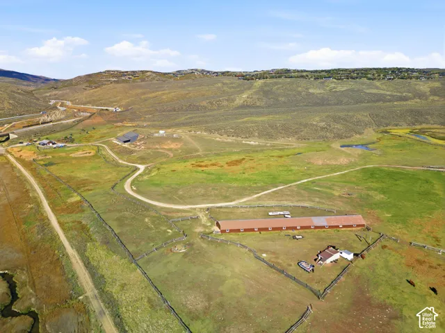 Expansive acreage featuring a long rectangular barn, perimeter wood fencing, dirt access paths, and rolling hillside topography