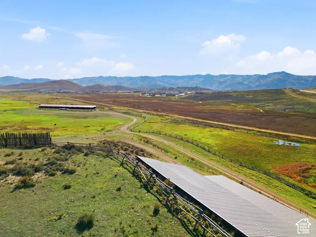Expansive acreage featuring rolling meadow terrain, mountain backdrop, wooden perimeter fencing, and a metal-roofed structure