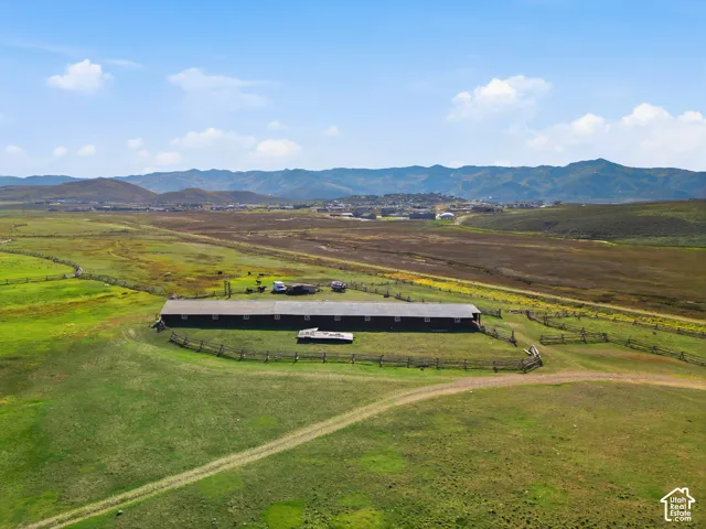 Expansive acreage featuring a long-span barn structure, perimeter split-rail fencing, open pasture land, and a mountain range backdrop