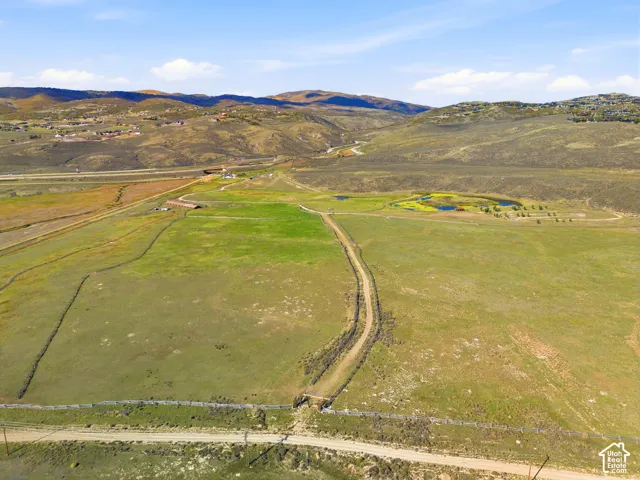 Expansive acreage featuring rolling terrain, a natural pond, perimeter fencing, and mountain scenery