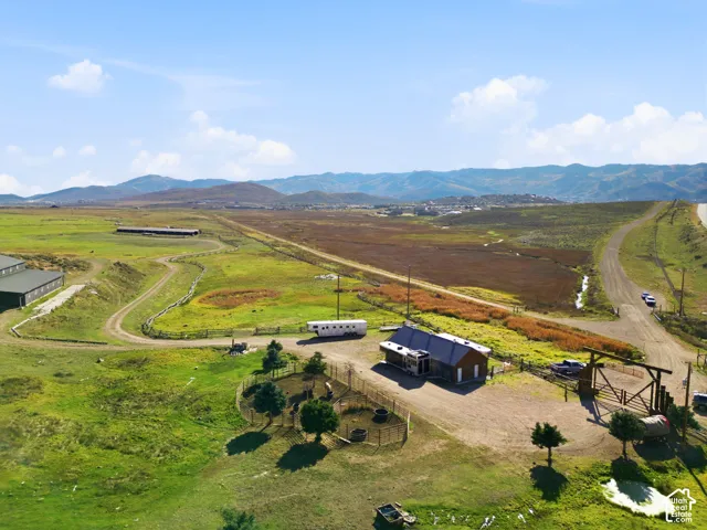 Expansive acreage featuring mountain silhouettes, fenced paddocks, a durable metal-roof outbuilding, and a timber-framed gated entry
