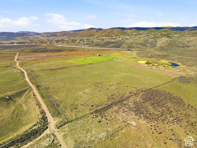 Expansive undeveloped acreage featuring rolling terrain, natural vegetation, perimeter fencing, and a permanent pond