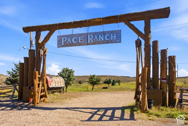 Custom timber-post entryway featuring a metal signage header and gravel-surfaced drive on expansive open acreage