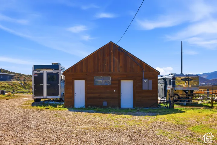 Gable-roof exterior structure featuring horizontal wood-plank siding, two individual entry doors, and a gravel lot