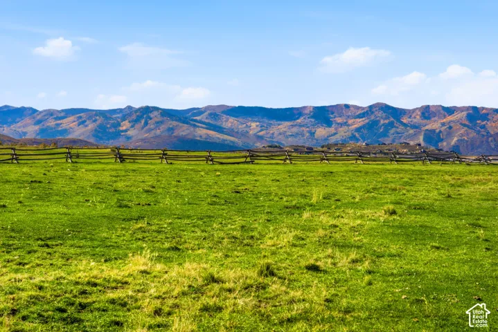 Expansive acreage featuring a natural grass field, split-rail fencing, and prominent mountain scenery