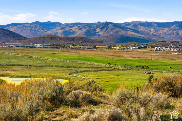 Expansive terrain featuring open meadowland, a natural pond, rustic split-rail fencing, and a prominent mountain range backdrop