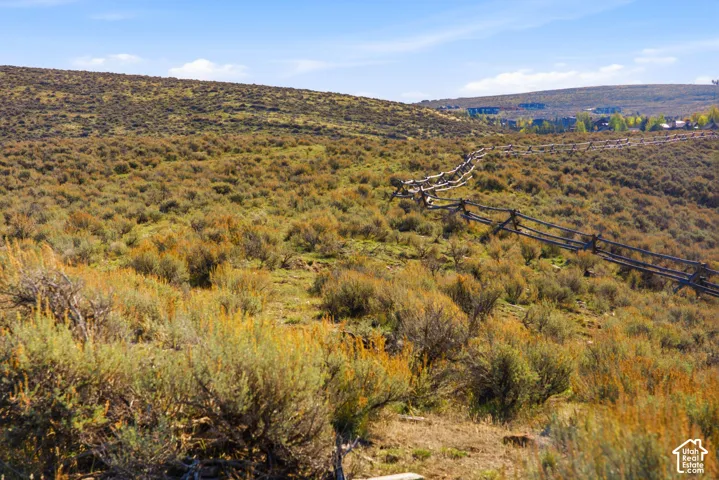 Expansive lot featuring rolling natural terrain, native shrubs, and a rustic split-rail wood fence