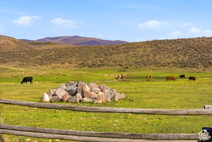 Expansive acreage featuring natural terrain, wooden split-rail fencing, a stone formation, and mountain scenery