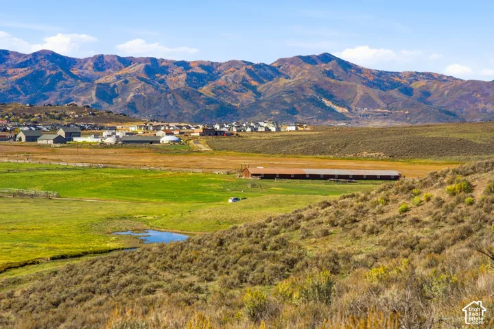 Expansive rural landscape featuring mountain backdrops, open green fields, native shrubbery, and a natural water feature