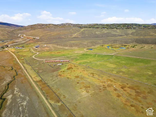 Expansive acreage featuring rolling mountain terrain, open pasture land, natural water features, and existing agricultural outbuildings