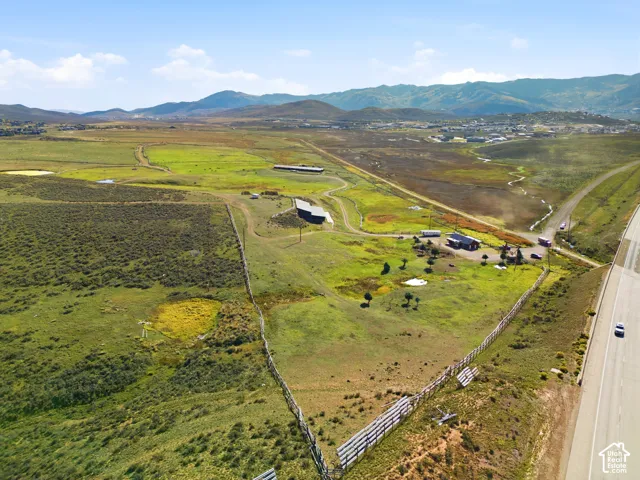 Expansive acreage featuring rolling terrain, mountain backdrops, perimeter fencing, and multiple outbuildings