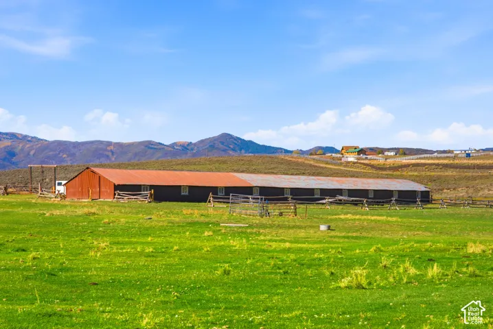Expansive pasture land featuring a long-form barn, rustic timber fencing, and mountain scenery