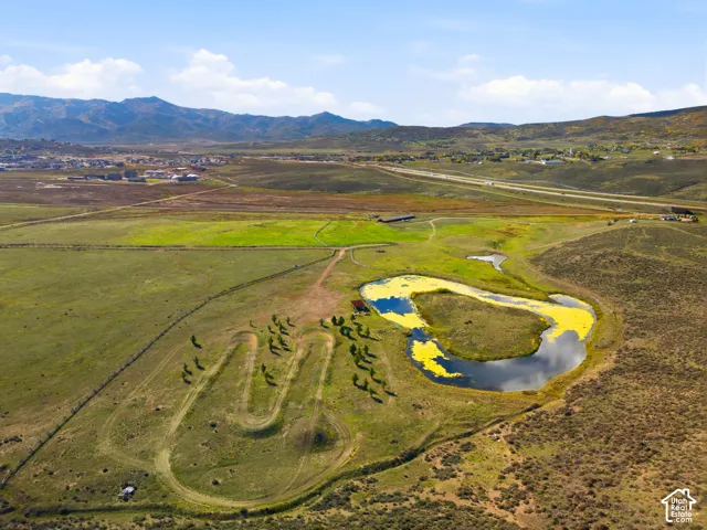 Expansive acreage featuring a natural pond, undulating terrain, mature tree groupings, and mountain backdrops
