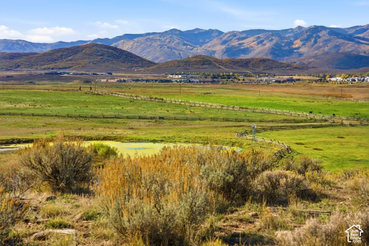 Expansive landscape featuring open meadow, native sagebrush, a small pond, and mountain range backdrop