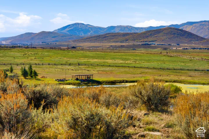 Expansive acreage featuring a natural pond, native brush vegetation, a wooden post-and-beam structure, and mountain scenery