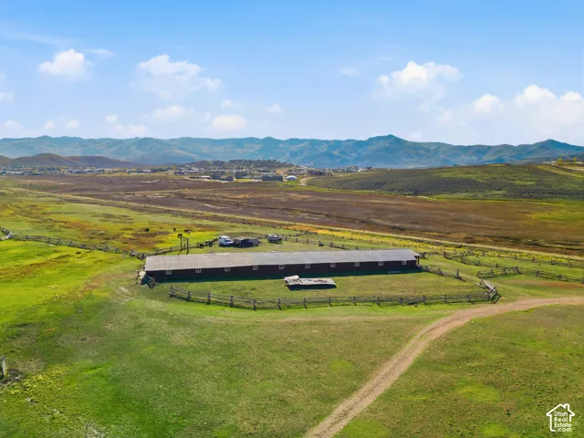 Expansive acreage featuring a long, single-story agricultural structure, fenced perimeter, and mountain backdrop